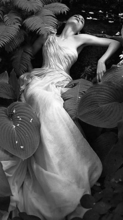 A Woman Laying On Top Of A Lush Green Field Next To Flowers And Plants