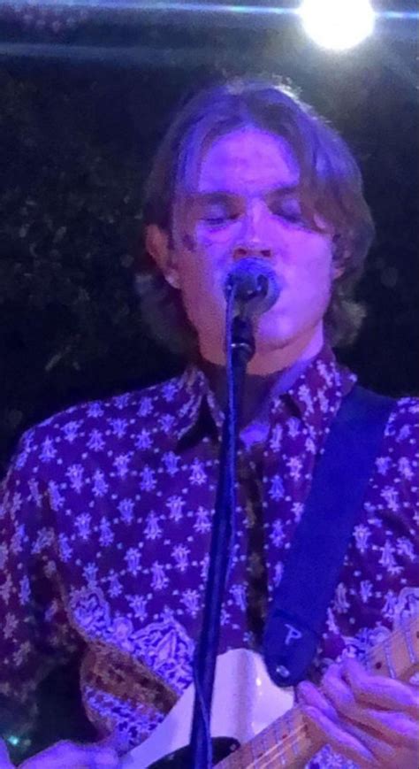 A Man With Glasses Playing Guitar In Front Of A Microphone