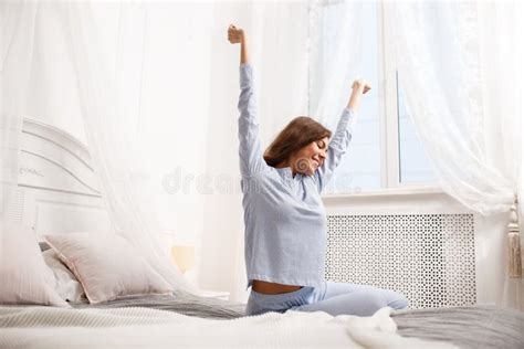 Happy Brunette Girl In The Light Blue Pajama Stretches Her Arms Up