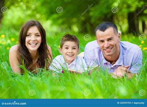 Famille De Trois Heureuse Se Trouvant Sur L Herbe Avec Le Livre Image