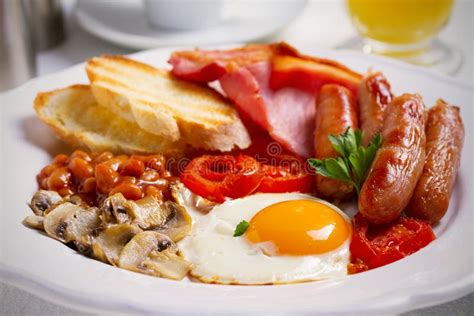 English Or Irish Breakfast In White Plate With Sausages Bacon Eggs Tomatoes Mushrooms