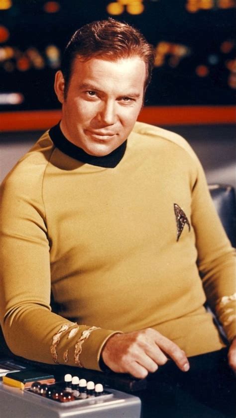 A Man In A Star Trek Uniform Sitting At A Desk With Control Buttons On It