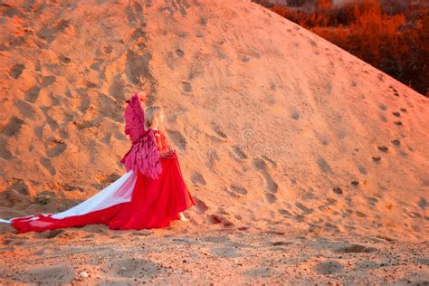 A Plump Blonde Middle Aged Woman With Red Angle Wings In A Desert With
