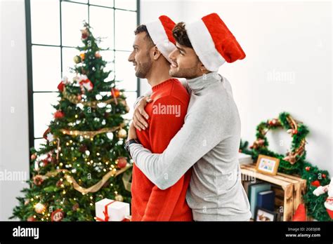 Joven pareja gay de pie por el árbol de Navidad con sombrero mirando hacia el lado perfil de