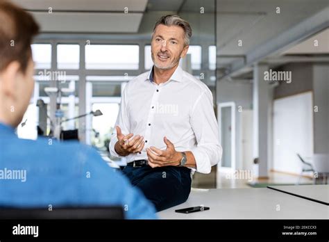 Mature Businessman Discussing With Colleague While Sitting At Office