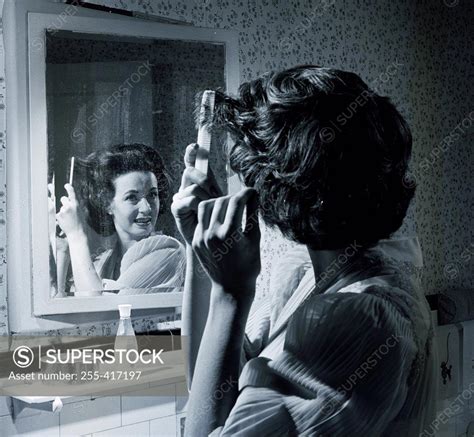 Woman Combing Hair In Front Of Mirror SuperStock