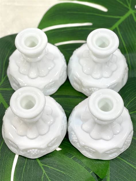 Four White Candle Holders Sitting On Top Of A Green Leaf