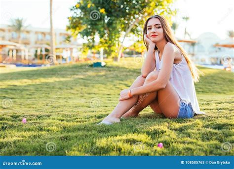 Beautiful Young Woman Sitting On The Grass In The Park On Sunshine