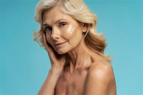 Premium Photo Beautiful Caucasian Blonde Mature Woman Applying Moisturizer On Face Blue