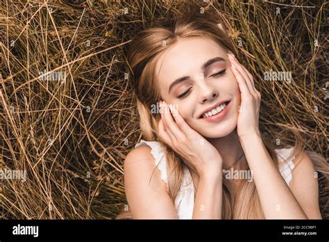 Top View Of Blonde Woman Touching Face While Lying On Green Grass With