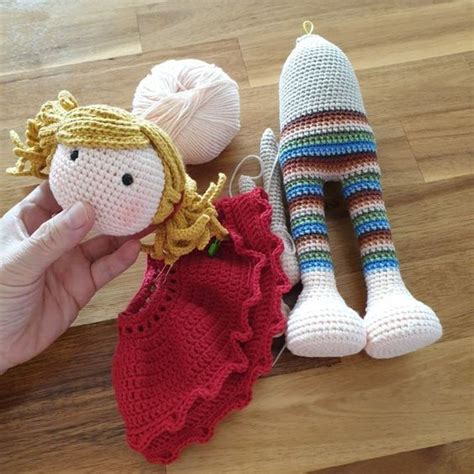 A Hand Holding Two Knitted Dolls Next To Each Other On A Wooden Floor