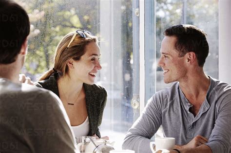 Three People Sitting At A Table Talking With Mugs And Jars Of