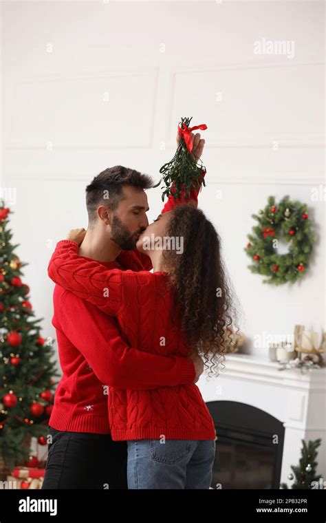 Happy Couple Kissing Under Mistletoe Bunch In Room Decorated For