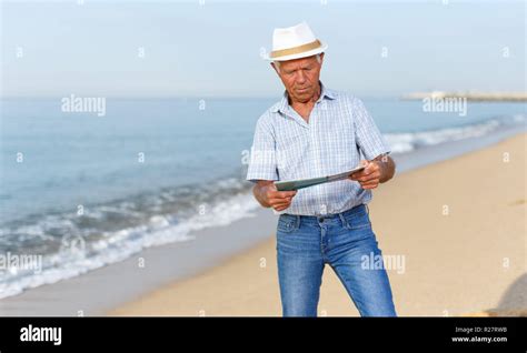 Positive Mature Man In Headwear Standing With Booklet Near Ocean Stock
