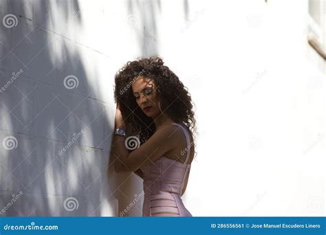 Beautiful Brunette Woman With Curly Hair Leaning Against A White Wall