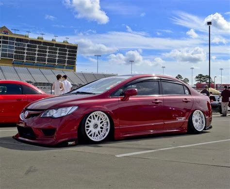 A Red Car Parked In A Parking Lot Next To Other Cars And People