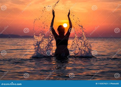 Silhouette Of Female Splashing Water With Her Hands At Sunset Over Sea