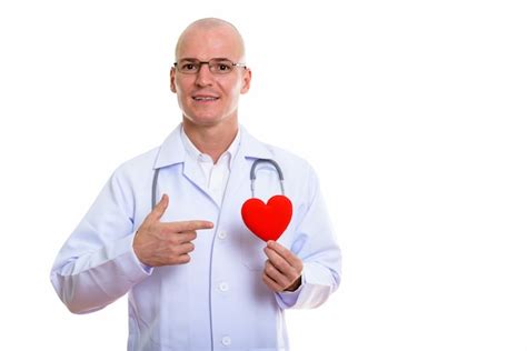 Joven médico calvo feliz sonriendo mientras sostiene el corazón Foto