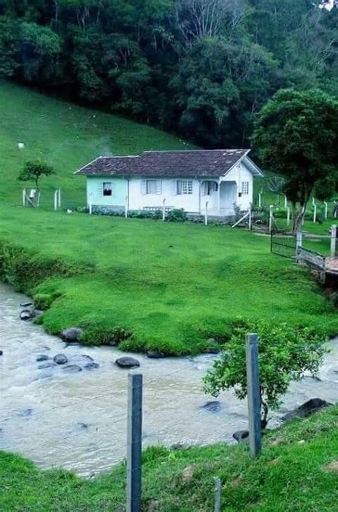 A White House Sitting On Top Of A Lush Green Hillside Next To A River