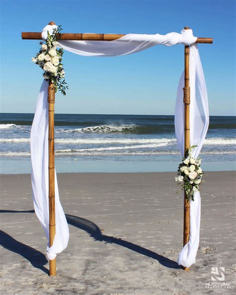 A Wooden Arch Decorated With White Flowers And Greenery Stands On The