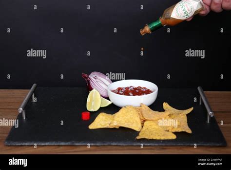 Hot Salsa Dip With Doritos Tortilla Chips And Tabasco Sauce Against Black Background Stock Photo