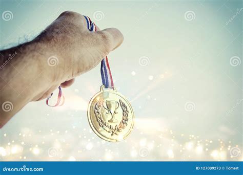 Man Hand Raised Holding Gold Medal Against Sky Award And Victory