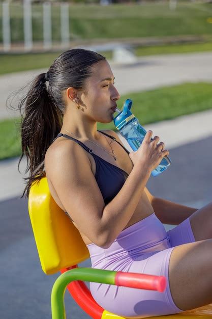 Premium Photo Athletic Latina Girl In Sportswear Drinking Water On An Exercise Machine In A