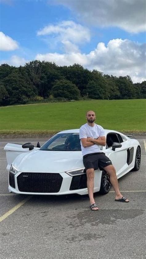 A Man Sitting On The Hood Of A White Sports Car In A Parking Lot With