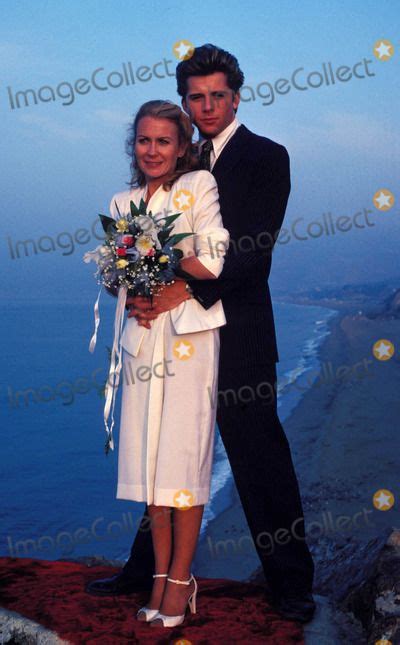 A Man And Woman Standing Next To Each Other On Top Of A Hill Near The Ocean