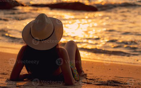 Back View Of Asian Woman Wear Bikini And Straw Hat Lying Down On Sand