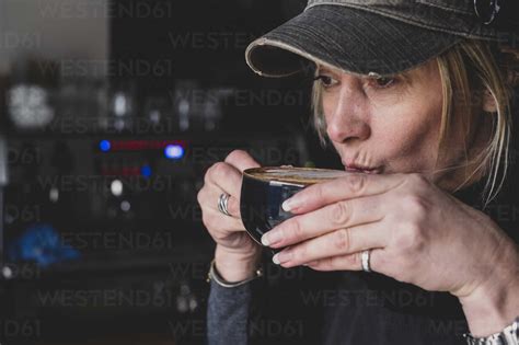 Close Up Of Blond Woman Wearing Baseball Cap Drinking Cappuccino Stock