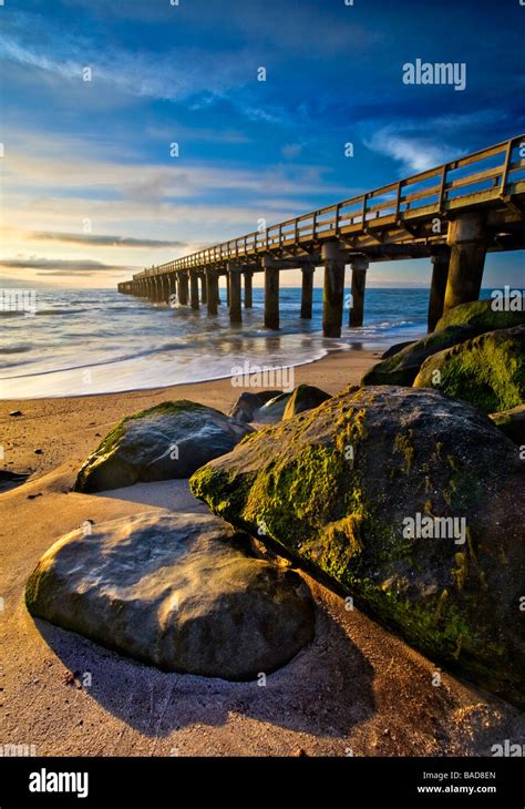 A Large Wooden Pier At Sunset With Rocks Covered In Green Moss All Lit