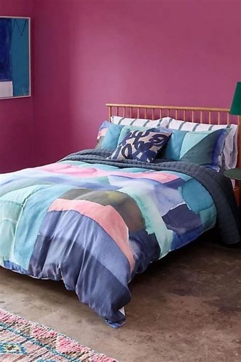 A Bed In A Room With Pink Walls And A Colorful Comforter On Top Of It