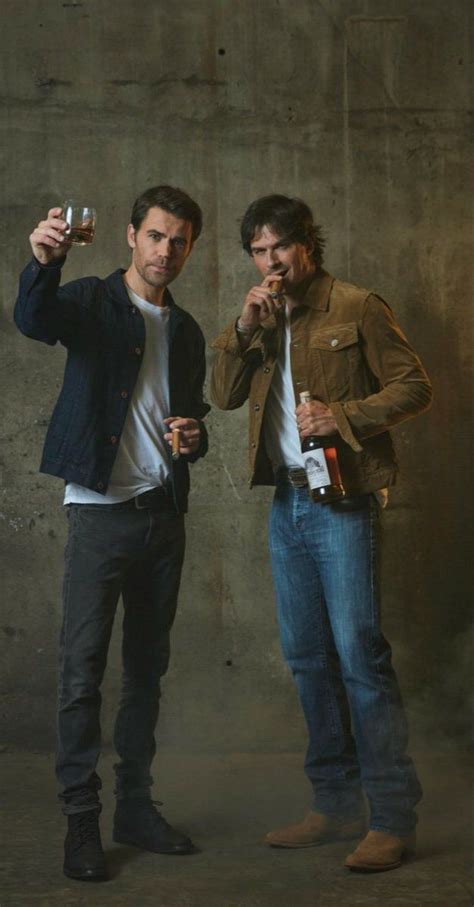 Two Men Standing Next To Each Other Holding Drinks