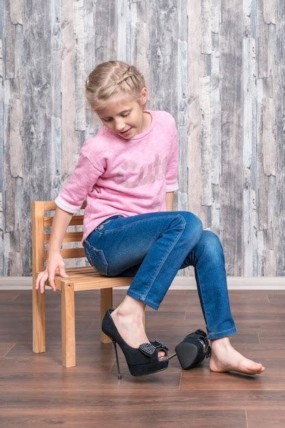 Une Fille Est Assise Sur Une Chaise En Bois Et Regarde Sa Jambe Vêtue