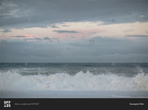 Waves breaking on the beach during dramatic sunset stock photo - OFFSET