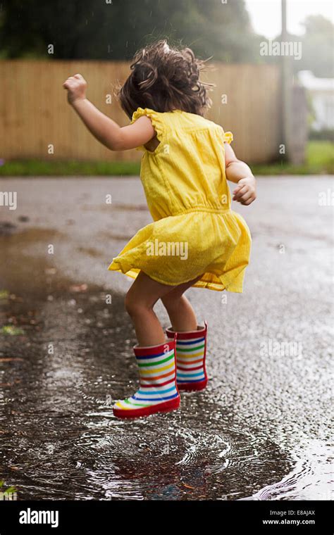 Girl Wearing Rubber Boots Jumping In Rain Puddle Stock Photo Royalty