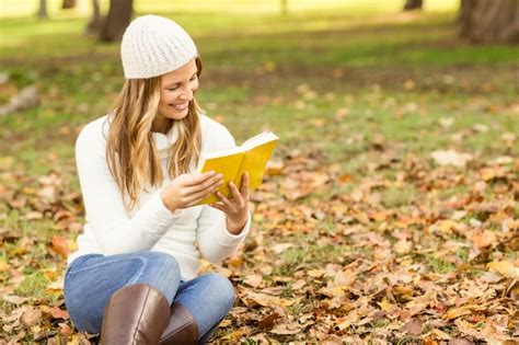 Sonriente Mujer Bonita Leyendo Un Libro En Hojas Foto Premium