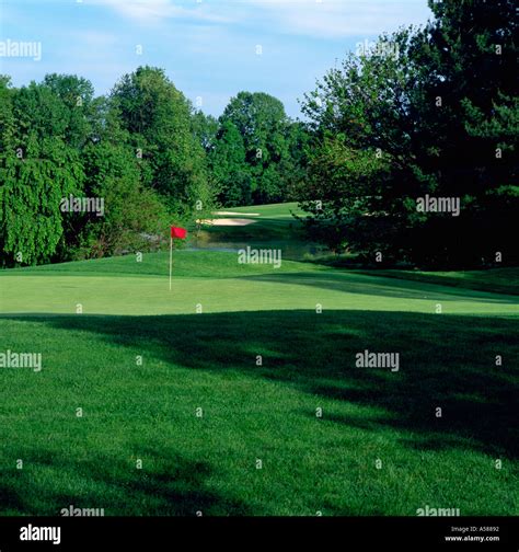 Red Flag Marks Hole Of Golf Green With Trees Pond And Sand Traps In