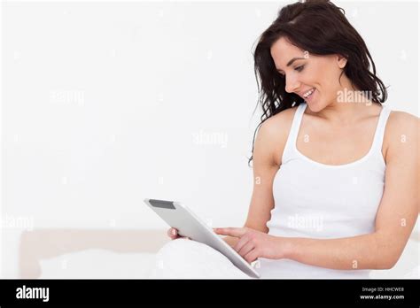 Smiling Brunette Woman Sitting While Using Her Touchscreen In Her
