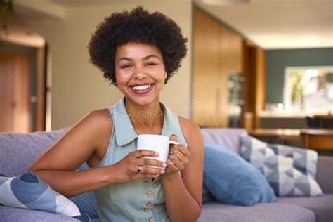 Portrait Of Smiling Woman Relaxing On Sofa At Home Holding Hot Drink Stock Photo Image Of Home