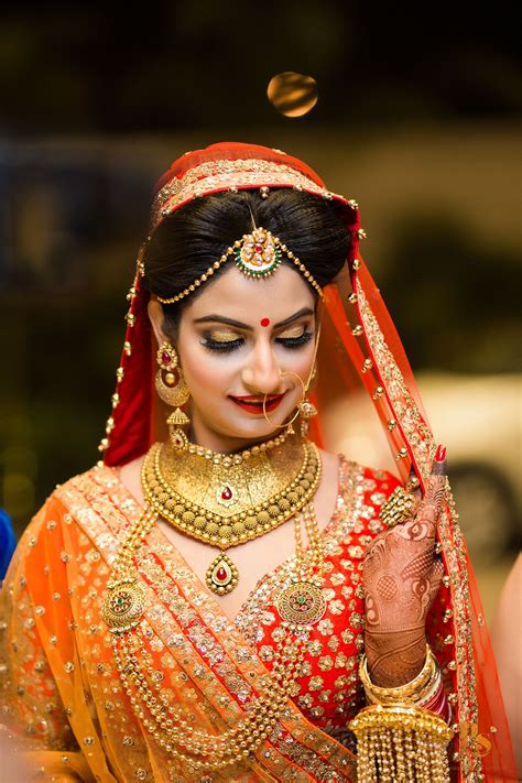 A Woman In An Orange And Red Bridal Outfit With Jewelry On Her Head Looking Down At The Ground