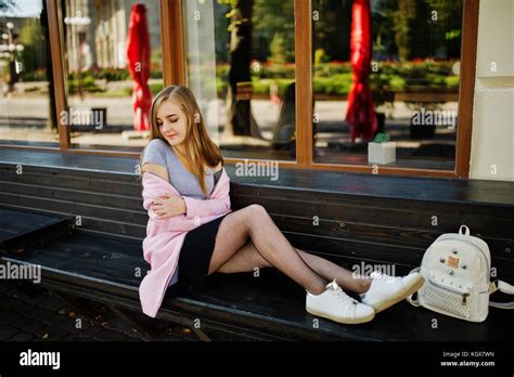 Jeune fille blonde en jupe noire et manteau rose avec sac à dos femme assis sur un banc en ville