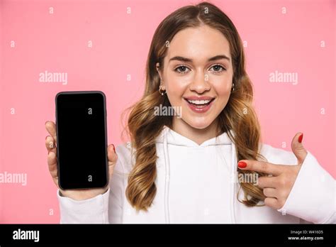 Happy Blonde Woman Wearing In Casual Clothes Showing Blank Smartphone Screen And Pointing On It