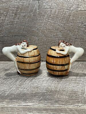 Two Ceramic Figurines Sitting On Top Of Wooden Barrels With Their Arms