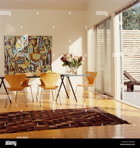 Large abstract painting on wall of modern white dining room with Arne Jacobsen "Ant"chairs and ...