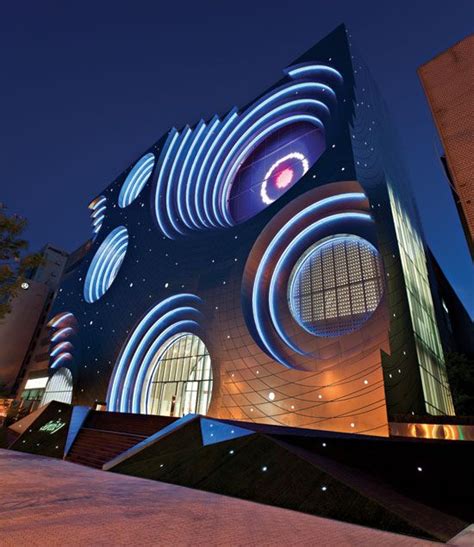 An Artistic Building Lit Up At Night With Blue And White Lights On The