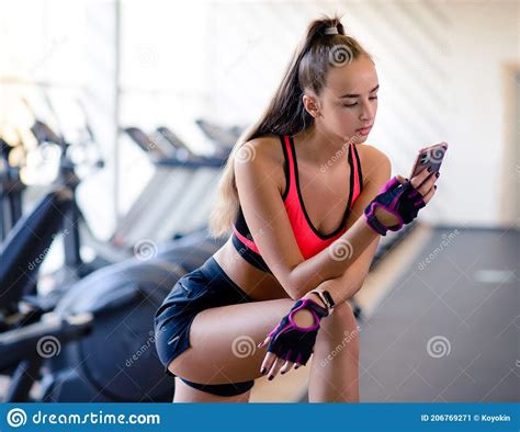 Attractive Athletic Girl In The Sportswear Uses The Fitness App On Your Smartphones In The Gym