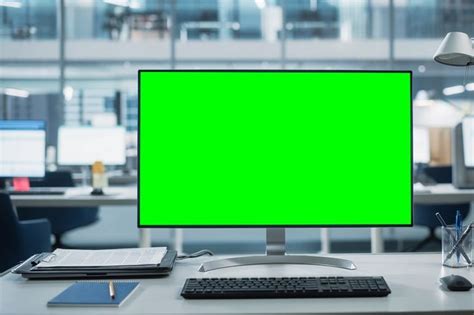 an office desk with a computer monitor, keyboard and notebook on it in front of a green screen