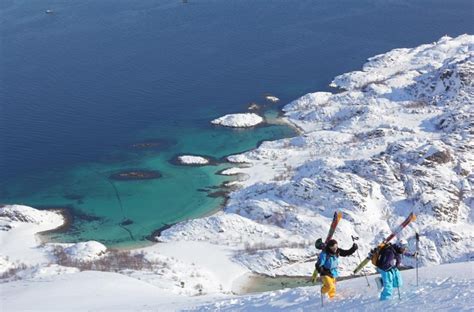 Two People With Skis Standing On Top Of A Snow Covered Hill Next To The